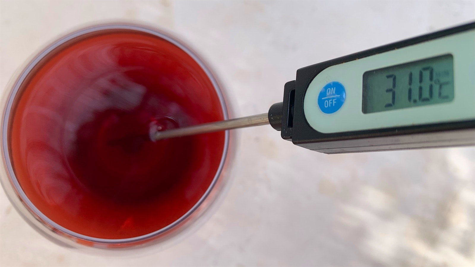A glass of red wine with a wine thermometer in it showing 31° C